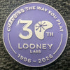 Round, metal pin with purple enamel featring 30th anniversary logo for Looney Labs in white lettering.